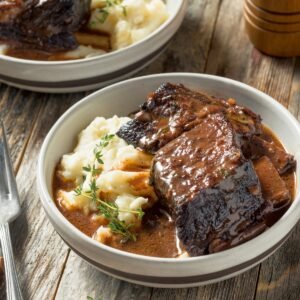 red wine braised short ribs served in a white bowl with mashed potatoes