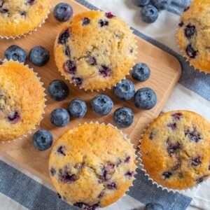 blueberry coconut muffins on a board surrounded by fresh blueberries